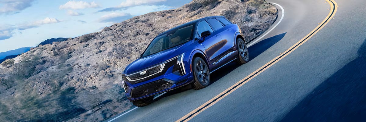 Blue 2027 Cadillac OPTIQ-V cornering on a two-lane highway