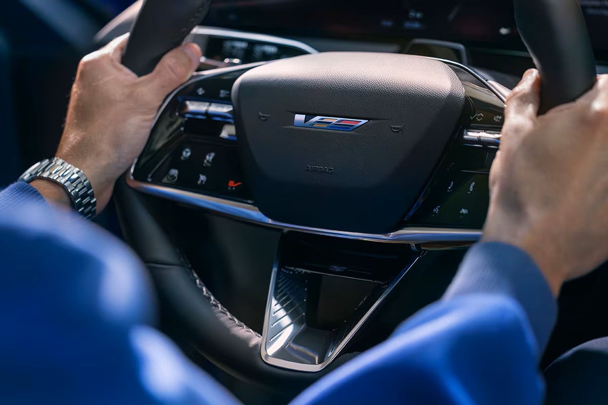Driver's hands on the V-Series steering wheel of a 2027 Cadillac OPTIQ-V